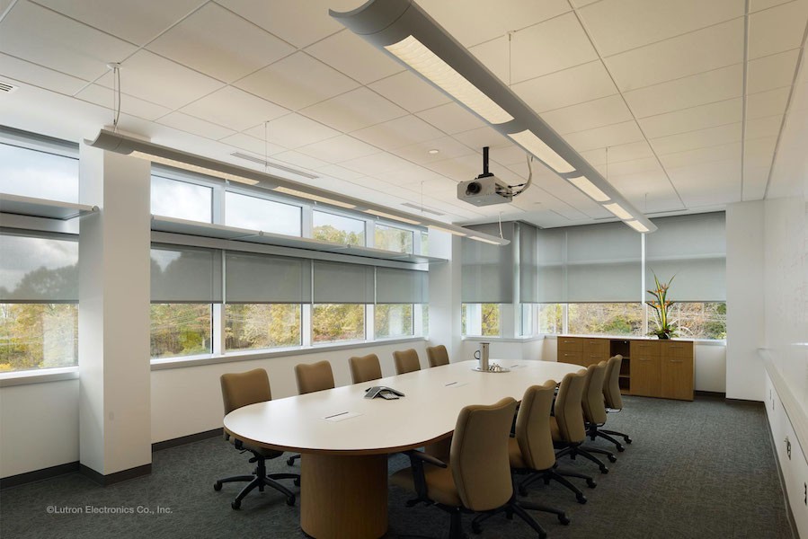 Conference room with yellow-toned lighting and motorized window shades.