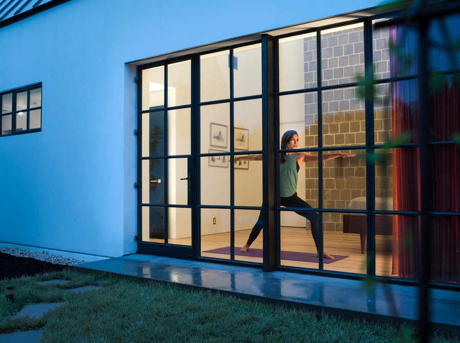 A woman practicing yoga behind her smart home’s large window.