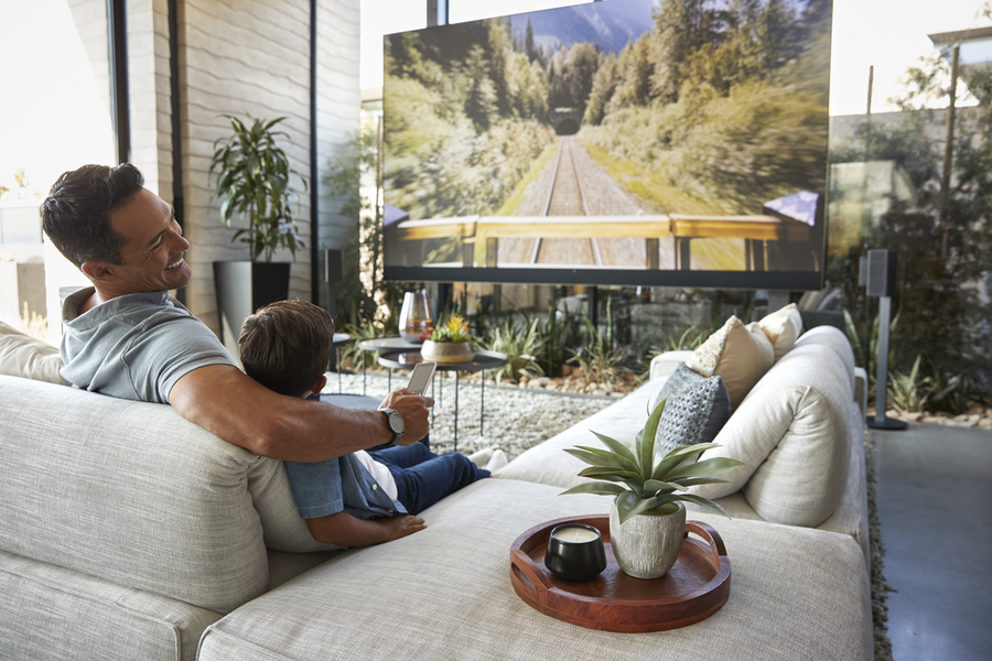 A man and his son happily watch TV and control content through a Savant system.
