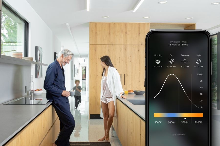 Couple in the kitchen with a phone screen in the forefront showing Savant interface. 