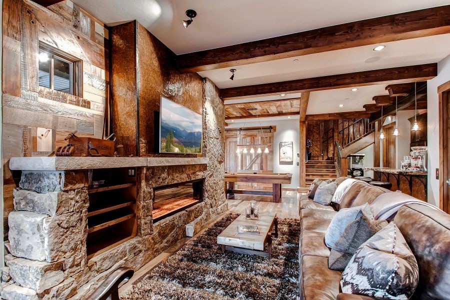  A living room with wooden beams, in-ceiling speakers, a TV above a fireplace, and a pool table.